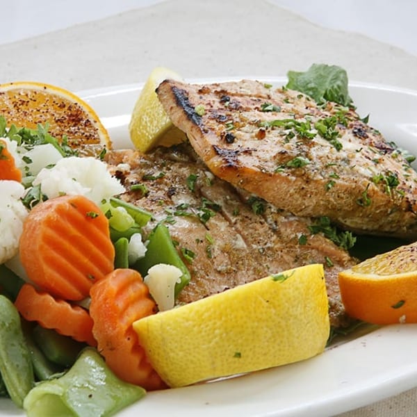 Grilled fish fillets with lemon and orange slices, served with steamed carrots, green beans, and cauliflower.