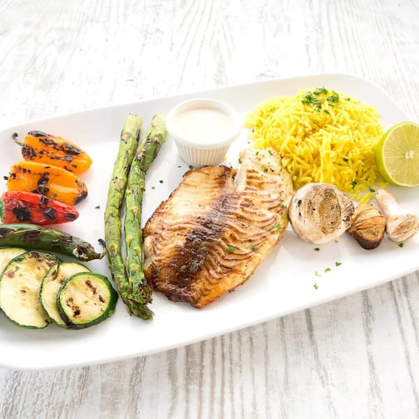 Grilled fish fillet with yellow rice, asparagus, zucchini, peppers, mushrooms, and a lime wedge.