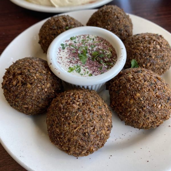 Six crispy falafel balls arranged around a small bowl of white sauce with herbs and spices.