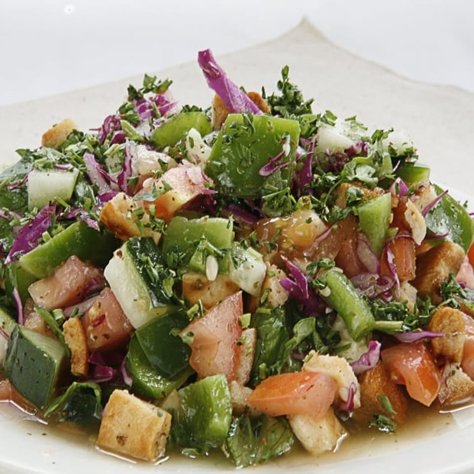Close-up of a vibrant Fattoush salad with fresh vegetables, herbs, and toasted bread pieces.