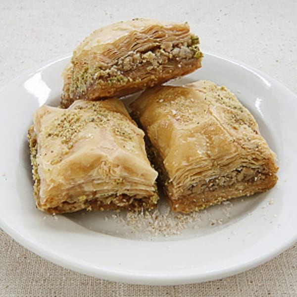 Three pieces of Hala In Restaurant's baklava, a middle-eastern dessert, on a white plate.
