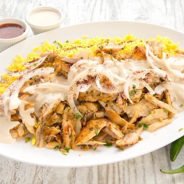 Hala In Restaurant's chicken shawarma plate with yellow rice, onions, white sauce, and two dipping sauces.