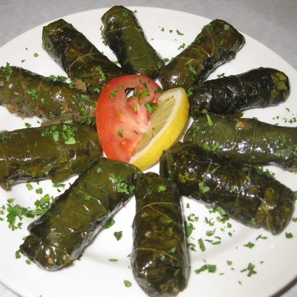 Hala In Restaurant's middle-eastern dolmas, garnished with parsley, tomato, and lemon on a white plate.