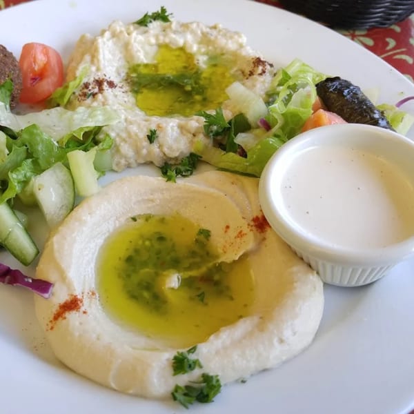 Two servings of hummus and baba ghanoush with olive oil, salad, and a side of tahini sauce.
