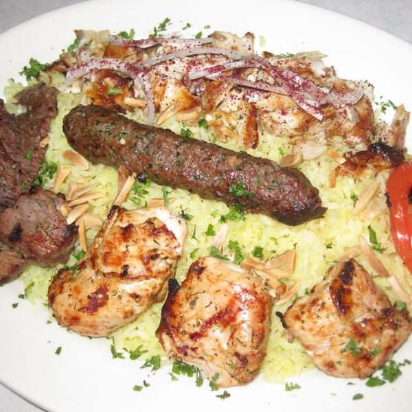 Hala In Restaurant's mixed grill platter with rice, beef, chicken, and kofta, garnished with parsley and almonds.